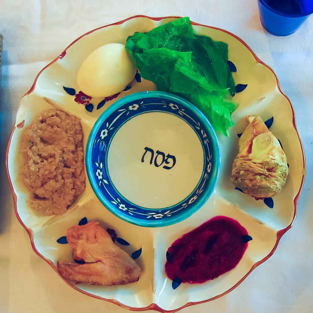 Zeitgenössischer Seder-Teller mit sieben Vertiefungen, von denen bis auf die mittlere größere Vertiefung alle mit Speisen gefüllt sind.